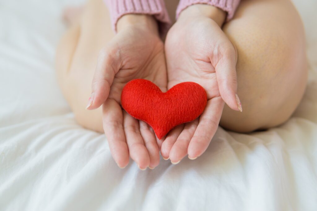 person kneeling on white bed holding red cloth heart in open hands to promote heart healthy snacking and heart month